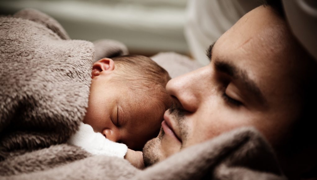Uomo che dorme con suo figlio in braccio.