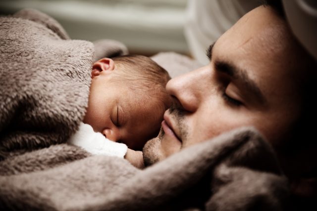 Uomo che dorme con suo figlio in braccio.